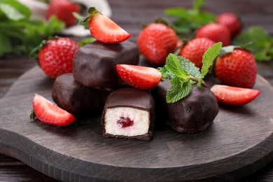 Photo of Delicious glazed curd snacks, mint leaves and fresh strawberries on wooden table, closeup