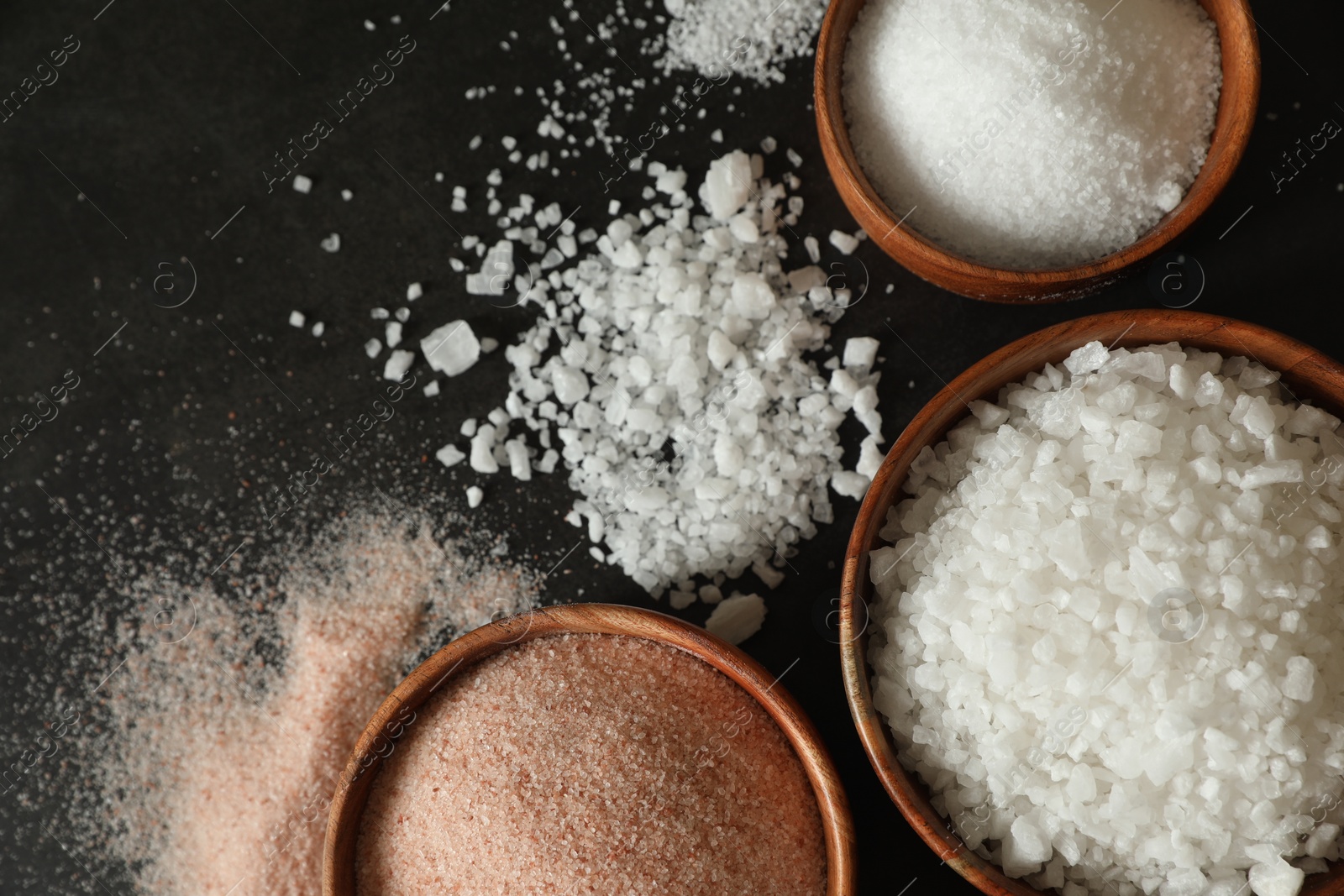 Photo of Different types of organic salt in bowls on black table, flat lay