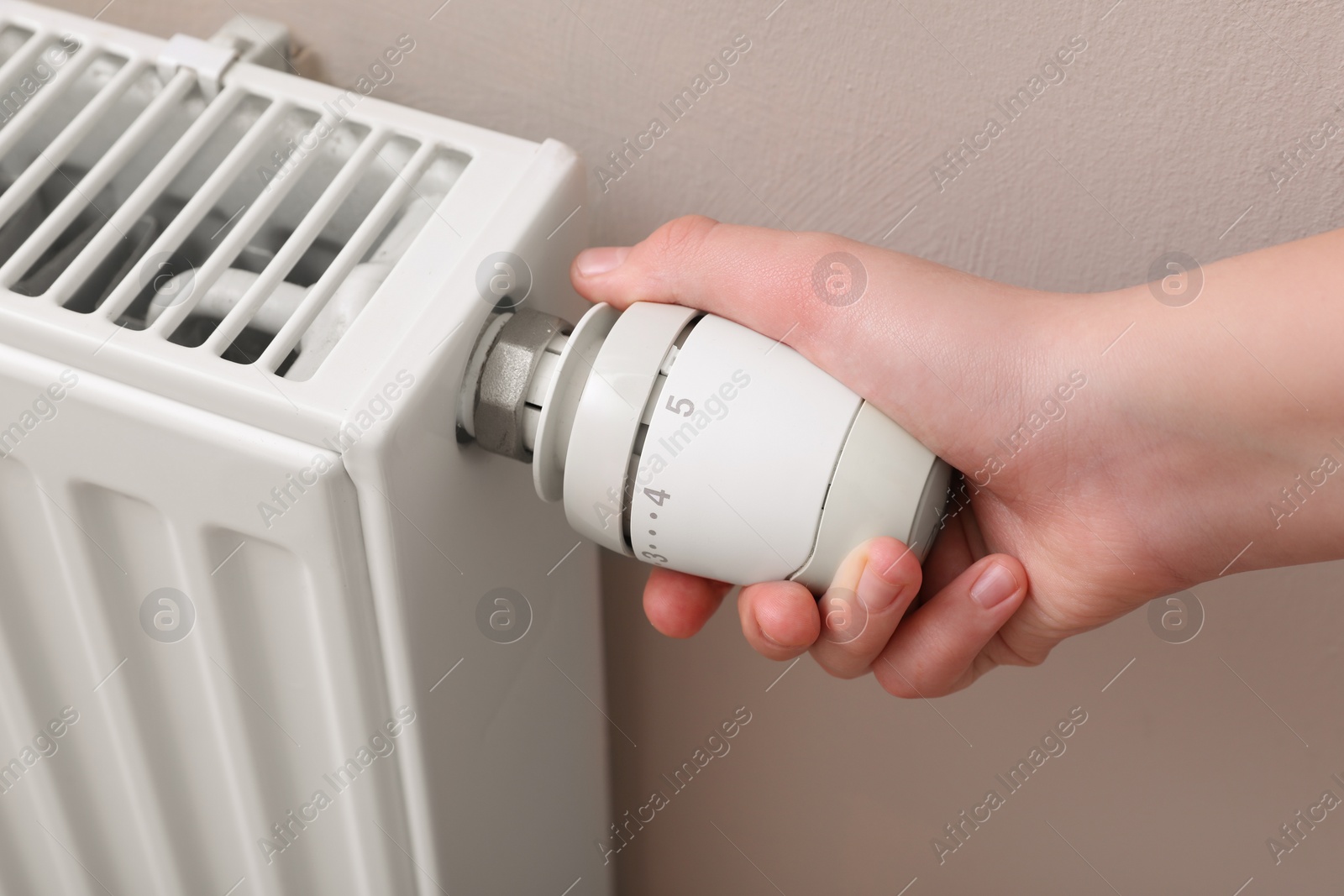 Photo of Girl adjusting heating radiator thermostat near white wall, closeup