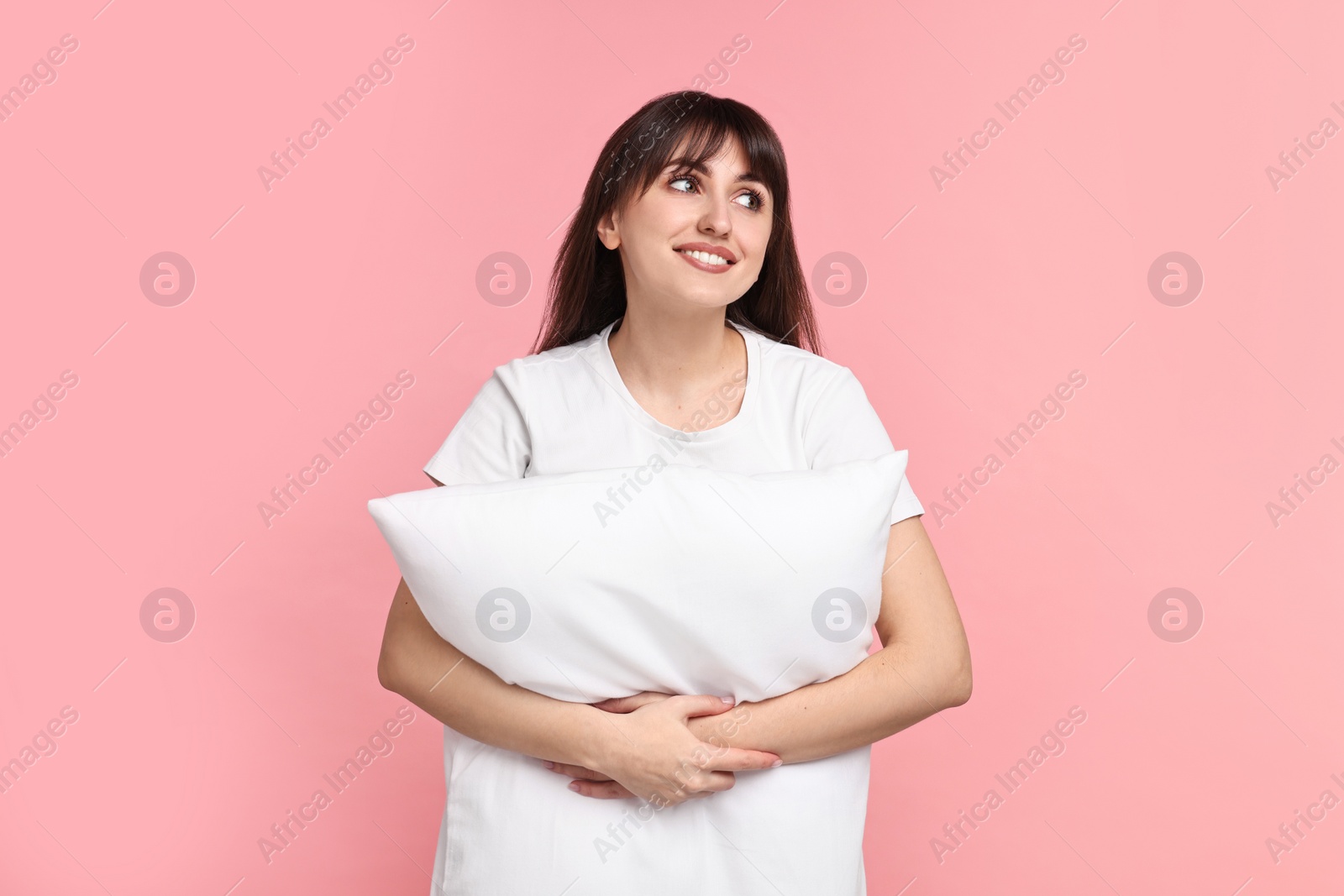 Photo of Happy woman in pyjama holding pillow on pink background