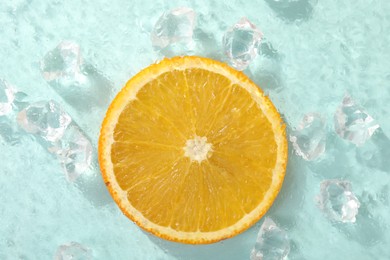 Slice of juicy orange and ice cubes on light blue background, top view