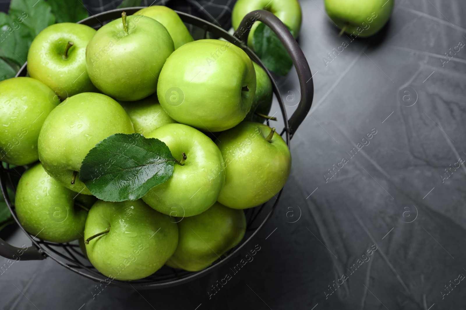 Photo of Juicy green apples in metal basket on grey table, above view