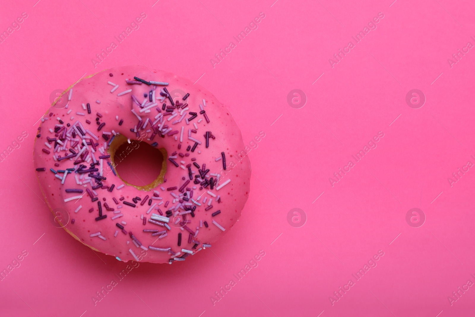 Photo of Sweet glazed donut decorated with sprinkles on pink background, top view and space for text. Tasty confectionery