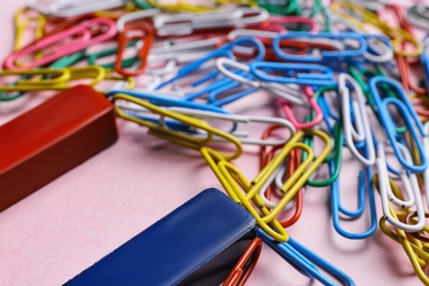 Red and blue horseshoe magnet attracting colorful paperclips on pink background, closeup