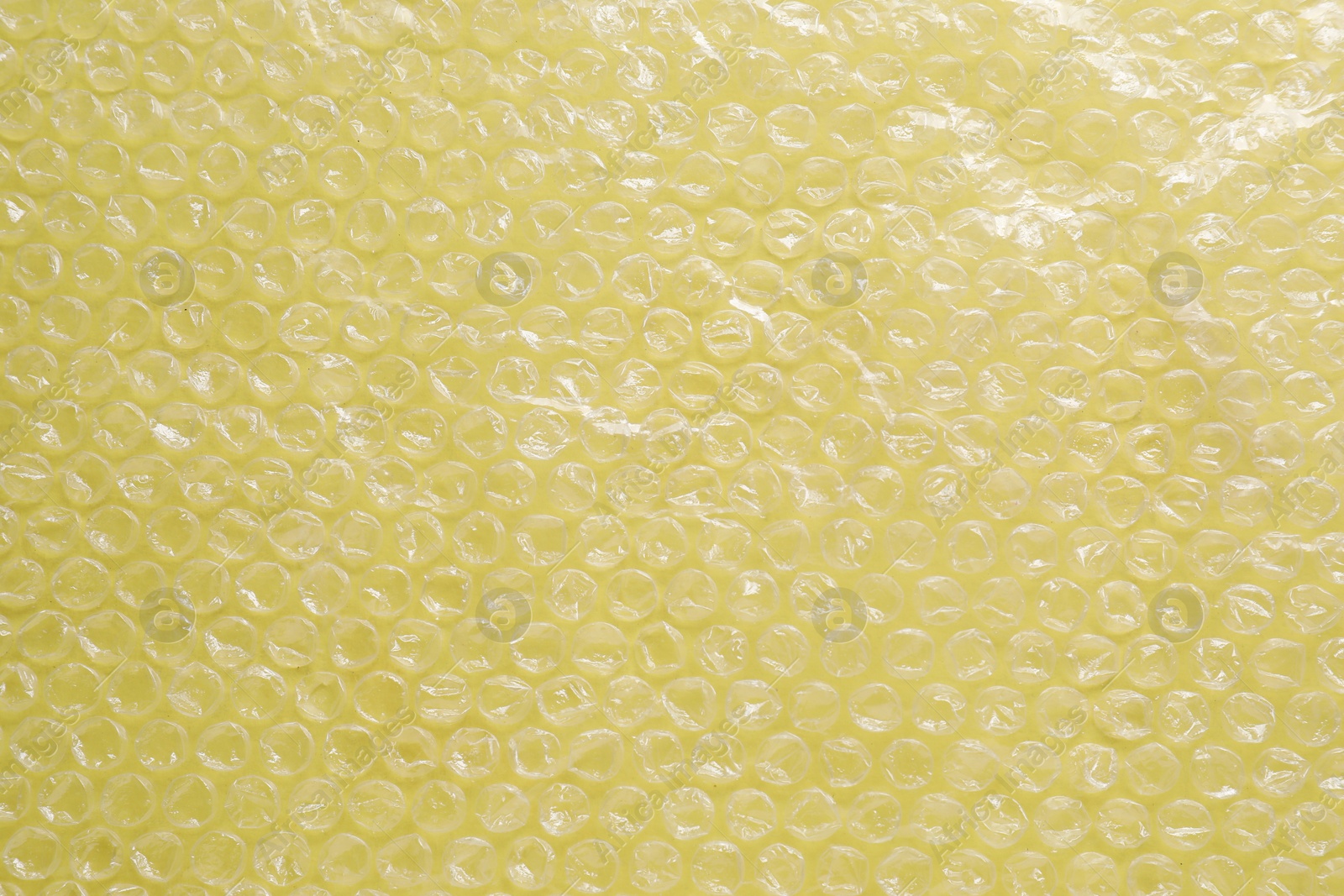 Photo of Transparent bubble wrap on yellow background, top view