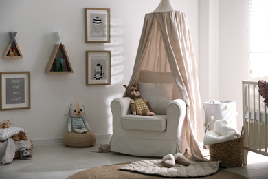 Stylish baby room interior with crib and comfortable armchair