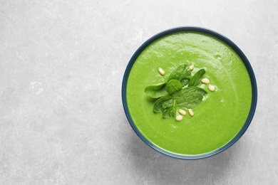 Photo of Bowl of healthy green soup with fresh spinach on grey table, top view. Space for text