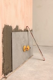 Photo of Construction level and yellow suction plate attached to tile on wall indoors
