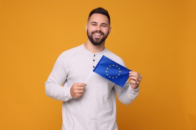 Photo of Young man holding flag of European Union on orange background