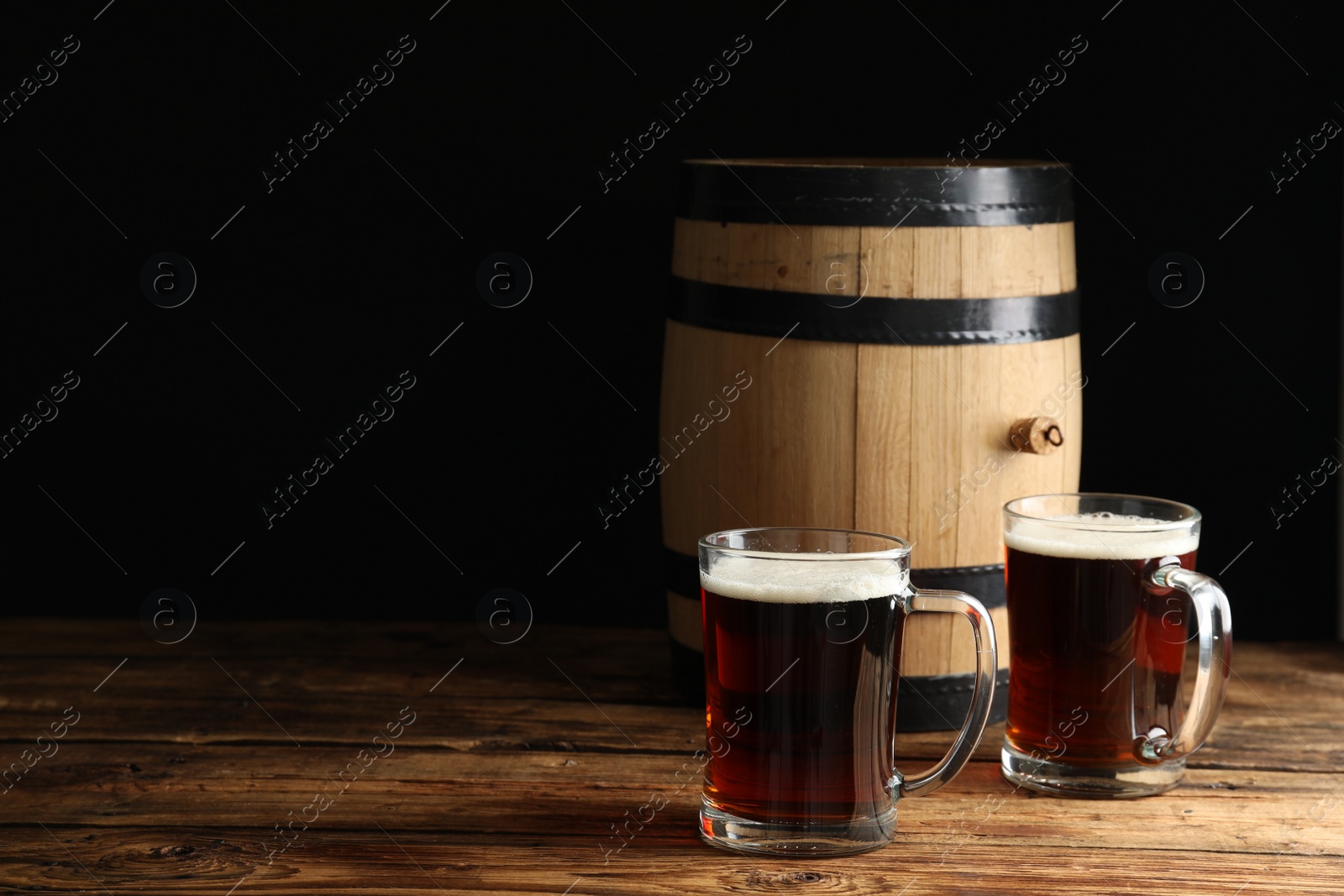 Photo of Glass mugs of delicious kvass and barrel on wooden table. Space for text