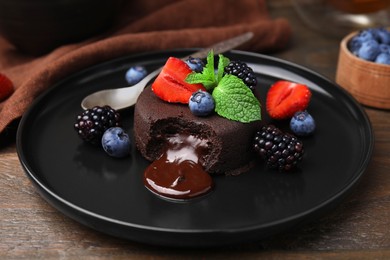 Photo of Plate with delicious chocolate fondant, berries and mint on wooden table, closeup