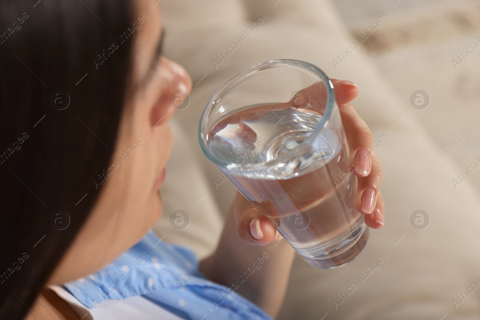Photo of Young woman drinking water on sofa, closeup. Refreshing drink
