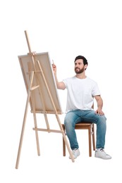 Photo of Man painting with brush against white background. Using easel to hold canvas