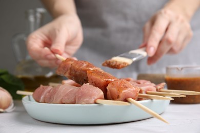 Photo of Woman spreading marinade onto raw meat with basting brush at table, closeup
