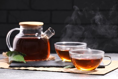 Aromatic hot tea in glass cups and teapot on light grey table near brick wall