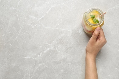 Woman holding Mason jar of melon ball cocktail with mint at light grey marble table, top view. Space for text