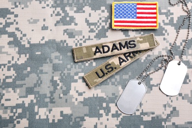 Photo of Military ID tags and US army patches on camouflage background, flat lay. Space for text
