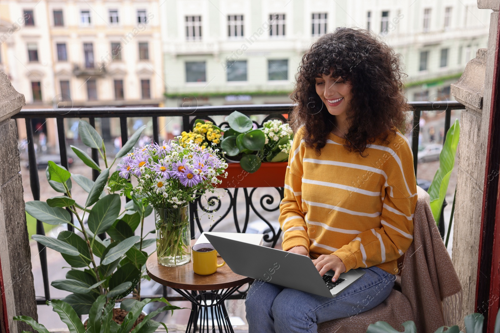 Photo of Beautiful young woman using laptop on balcony with green houseplants