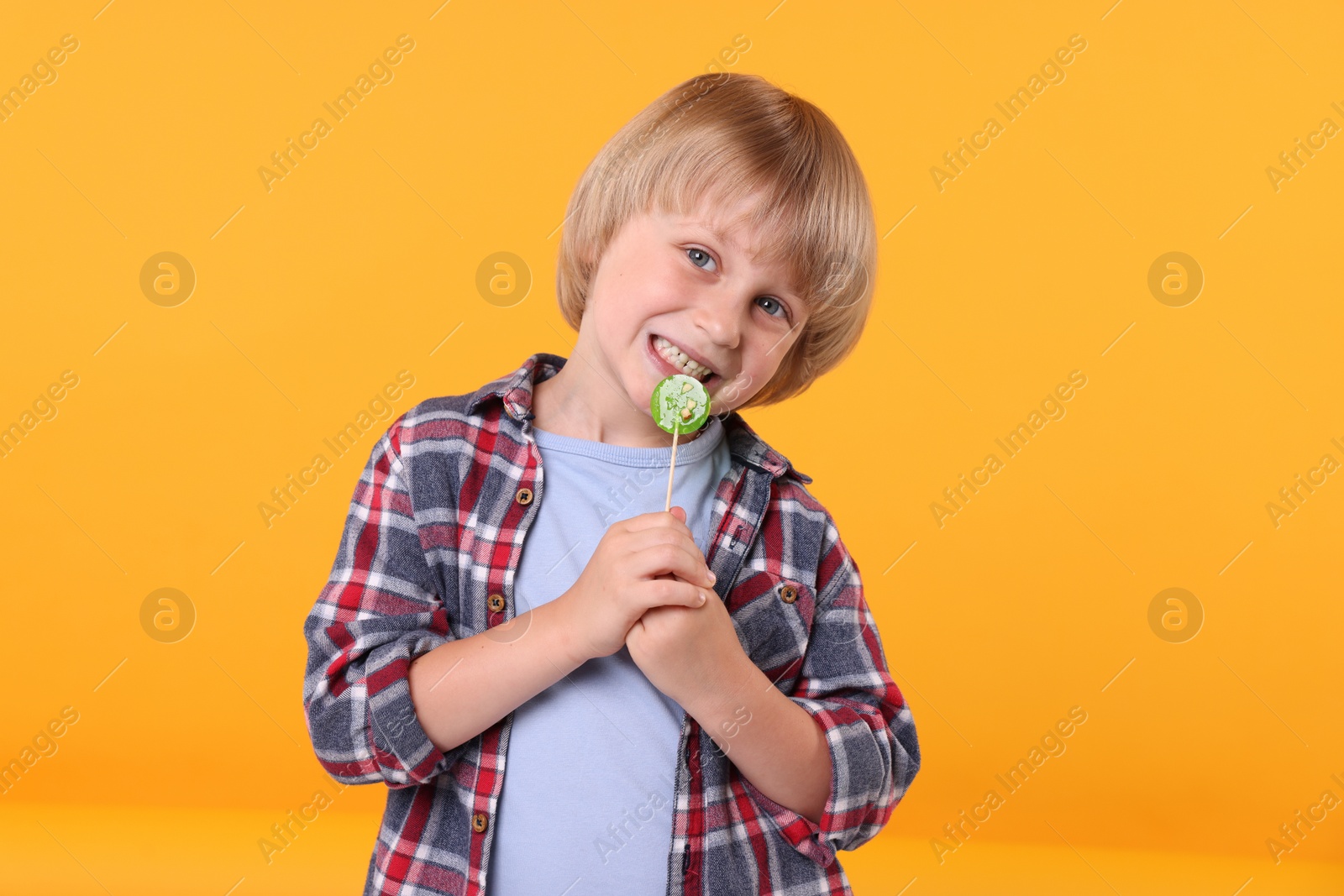 Photo of Cute little boy with lollipop on orange background