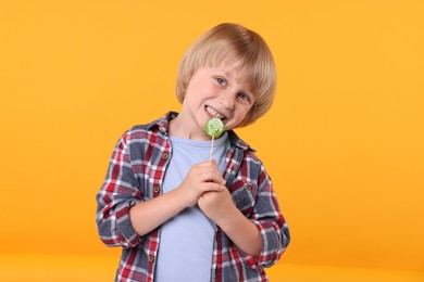 Photo of Cute little boy with lollipop on orange background