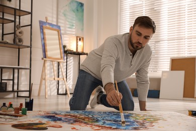 Photo of Young man painting on canvas with brush in artist studio