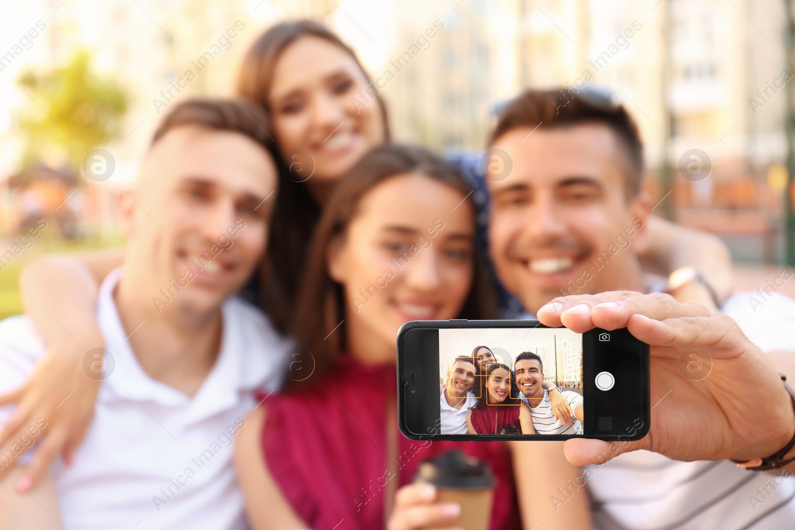 Photo of Group of young people taking selfie outdoors, focus on smartphone