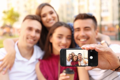 Photo of Group of young people taking selfie outdoors, focus on smartphone