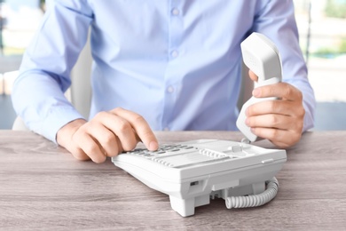 Photo of Man dialing number on telephone at workplace