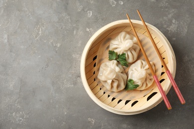 Photo of Bamboo steamer with tasty baozi dumplings and chopsticks on grey background, top view. Space for text