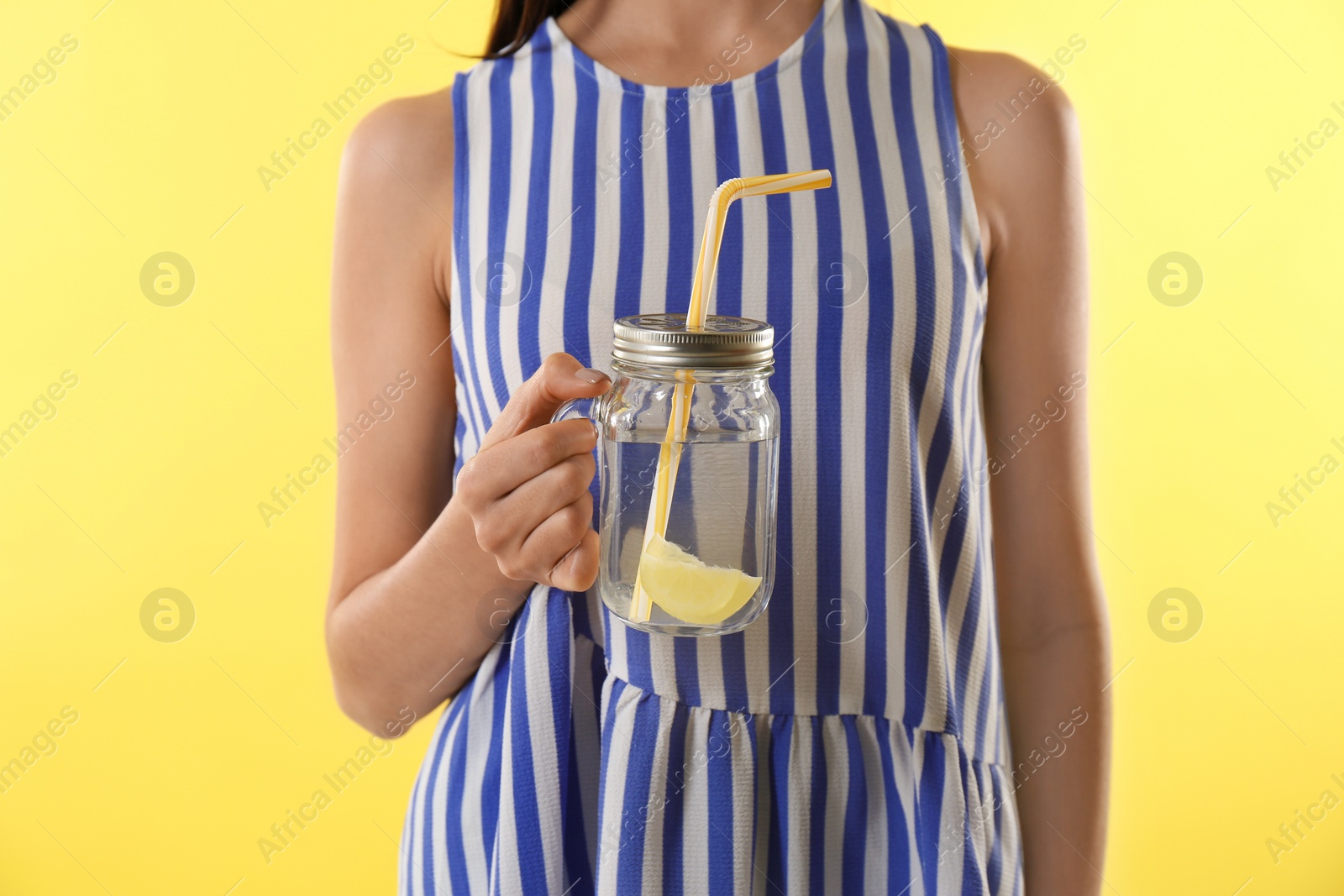 Photo of Young woman with tasty lemon water on yellow background, closeup