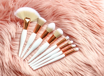 Photo of Set of makeup brushes on faux fur, flat lay