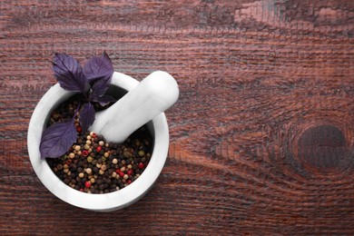 Photo of Mortar with peppercorns and basil on wooden table, top view. Space for text