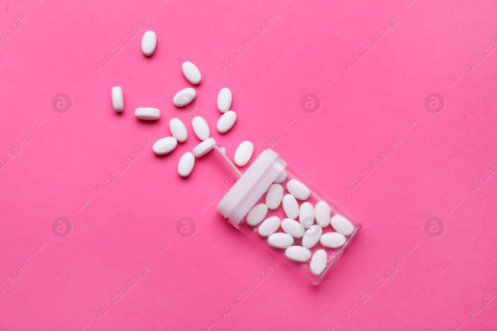 Photo of Tasty dragee candies and container on pink background, flat lay