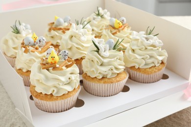 Photo of Tasty Easter cupcakes with vanilla cream in box on table, closeup