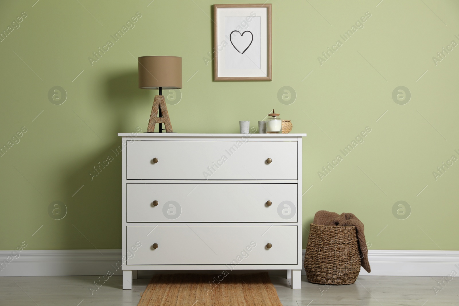 Photo of Modern white chest of drawers with lamp and decor near light green wall indoors