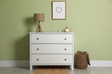 Photo of Modern white chest of drawers with lamp and decor near light green wall indoors