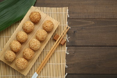 Photo of Delicious sesame balls, green leaf and chopsticks on wooden table, flat lay. Space for text