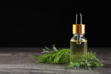 Photo of Bottle of essential oil and fresh dill on grey table, space for text