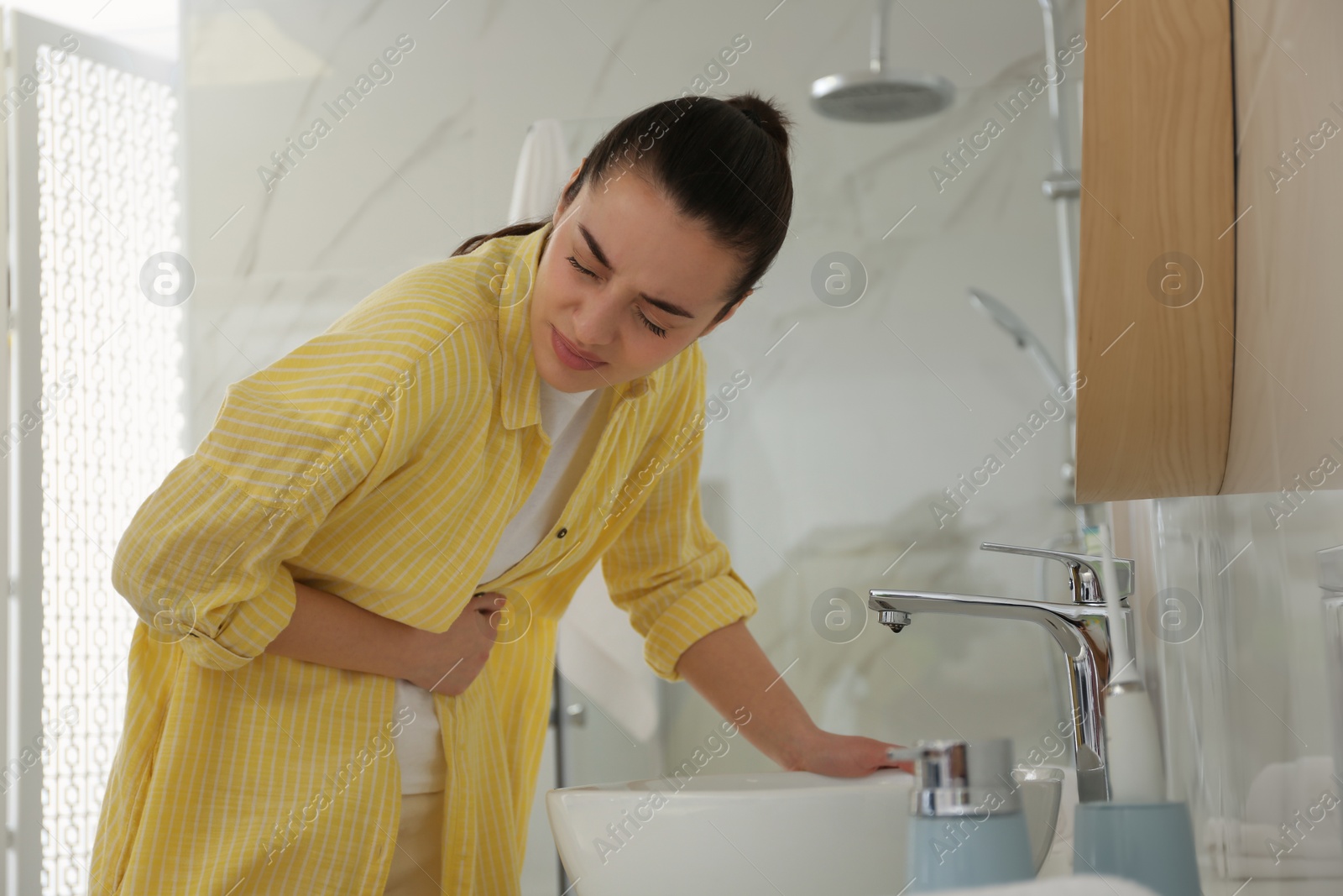 Photo of Young woman suffering from stomach ache in bathroom. Food poisoning