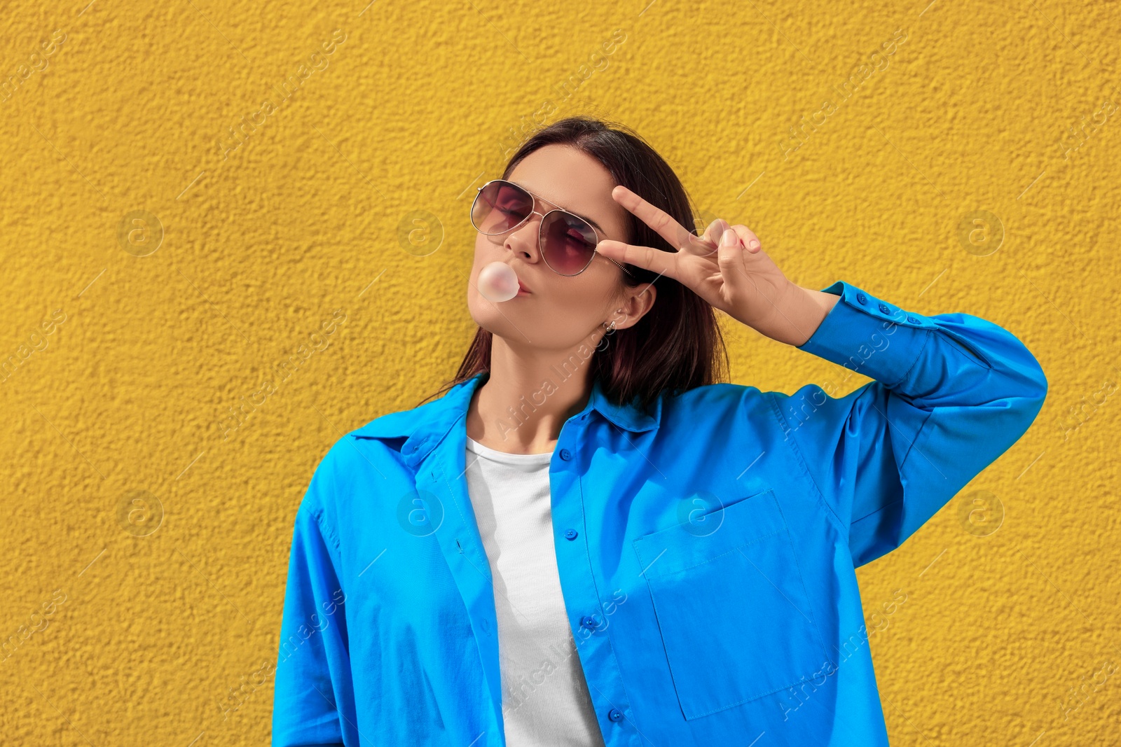 Photo of Beautiful young woman with sunglasses blowing chewing gum near orange wall