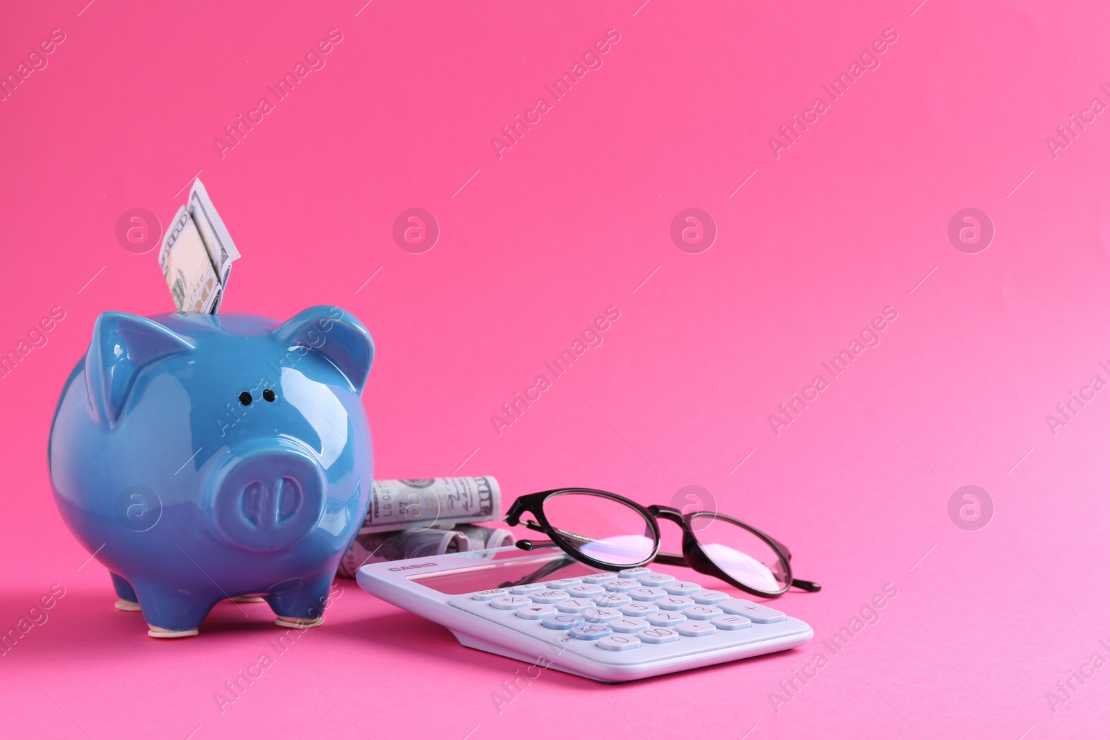 Photo of Financial savings. Piggy bank, dollar banknotes, glasses and calculator on pink background