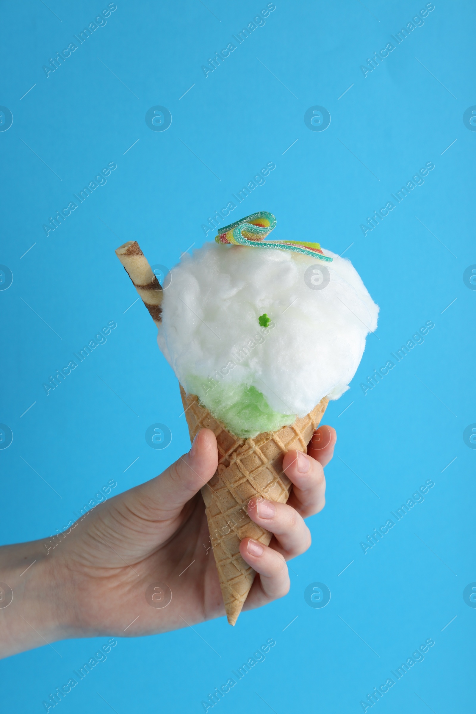 Photo of Woman holding waffle cone with cotton candy on light blue background, closeup