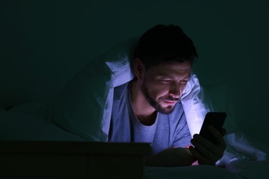 Man using smartphone under blanket in bed at night. Internet addiction