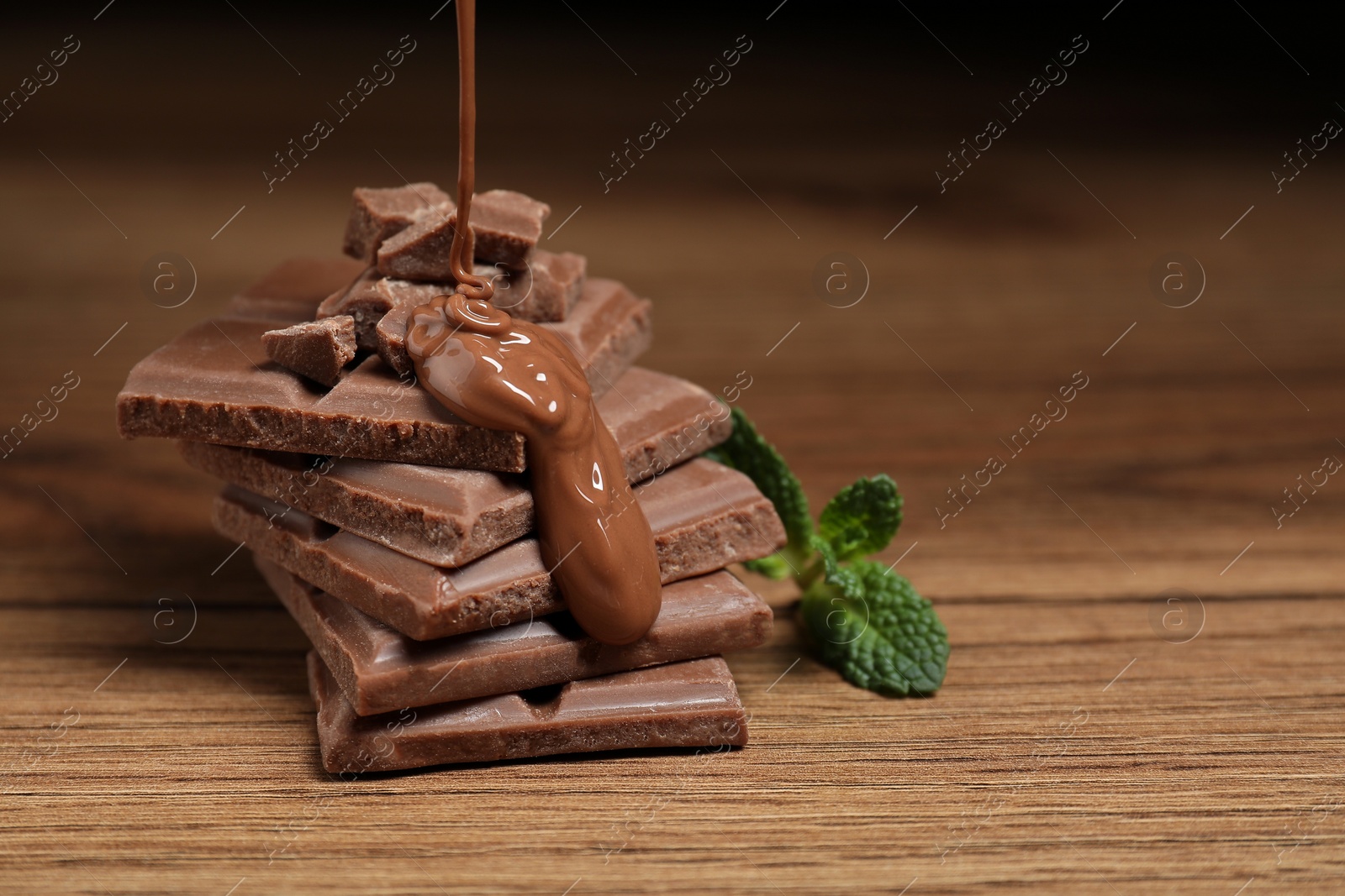 Photo of Pouring tasty milk chocolate paste onto pieces on wooden table, closeup. Space for text