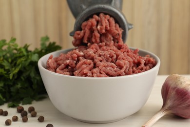 Photo of Mincing beef with manual meat grinder. Parsley, garlic and peppercorns on white table, closeup