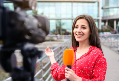 Image of Young female journalist with microphone working on city street