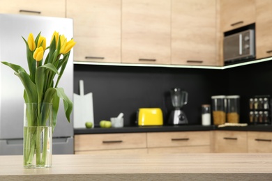 Photo of Glass vase with tulips on table in kitchen