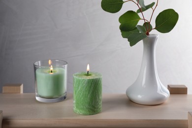 Scented candles near vase with eucalyptus branch on wooden table