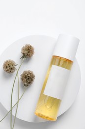 Bottle of cosmetic product, dried flowers and round podium on white background, top view