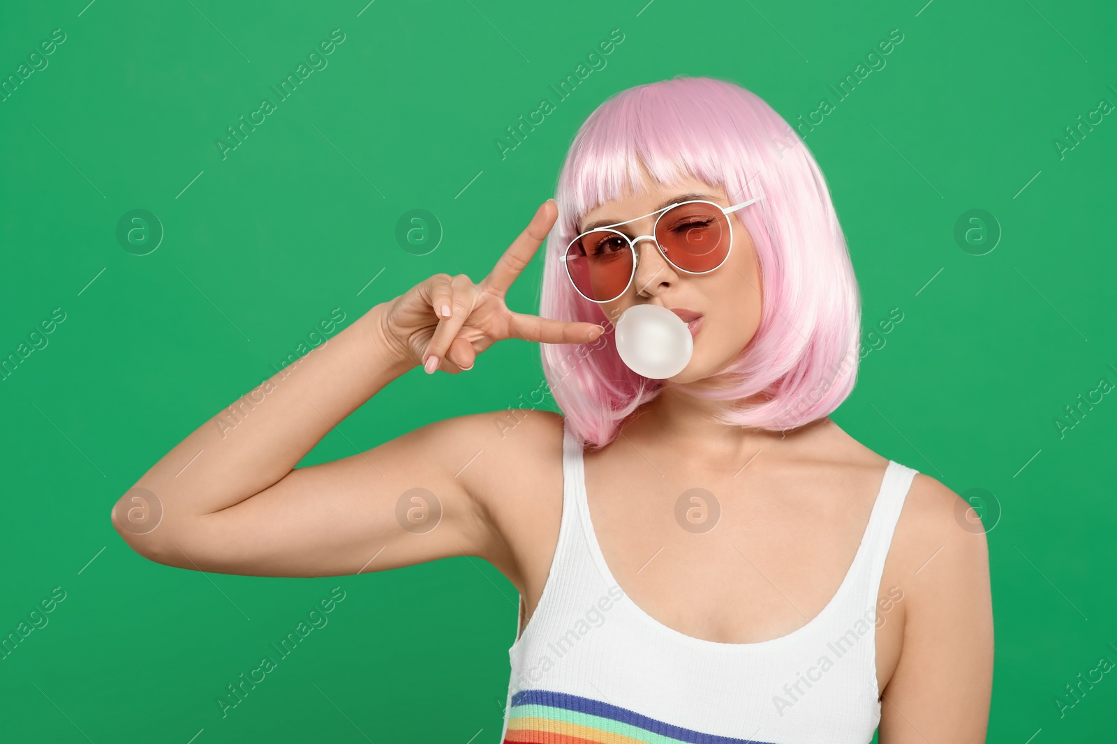 Photo of Beautiful woman in sunglasses blowing bubble gum and gesturing on green background